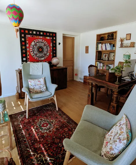 Cabinet de sophrologie avec deux grands fauteuils et un tapis oriental, ambiance chaleureuse, beaucoup de bois dans la pièce ce qui vient la réchauffer